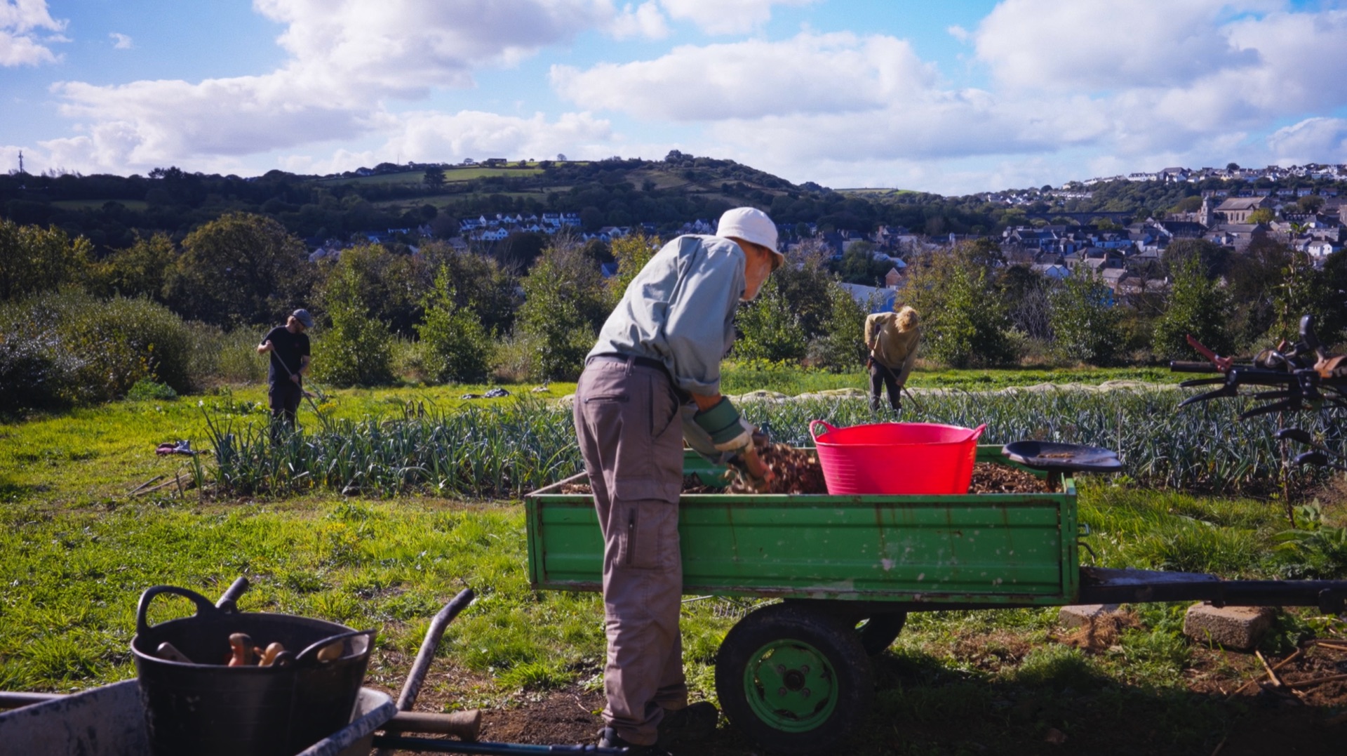 Volunteers working at Loveland Market Garden with houses on the hillside beyond, Cornwall